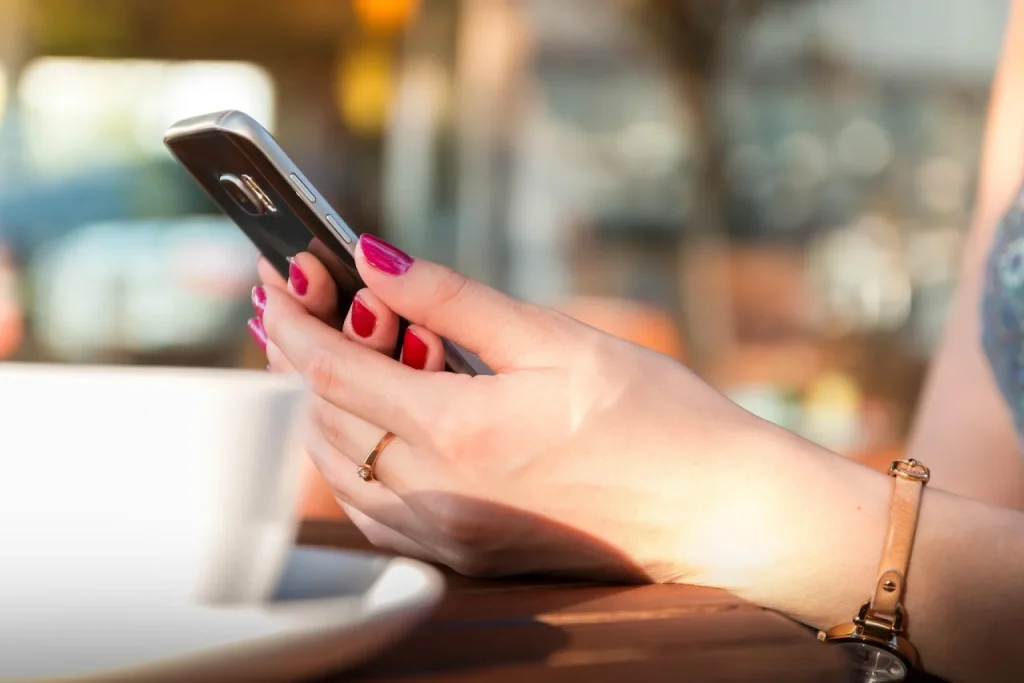 Dona de loja de cosméticos consulta anotações de clientes no balcão enquanto responde mensagens no celular